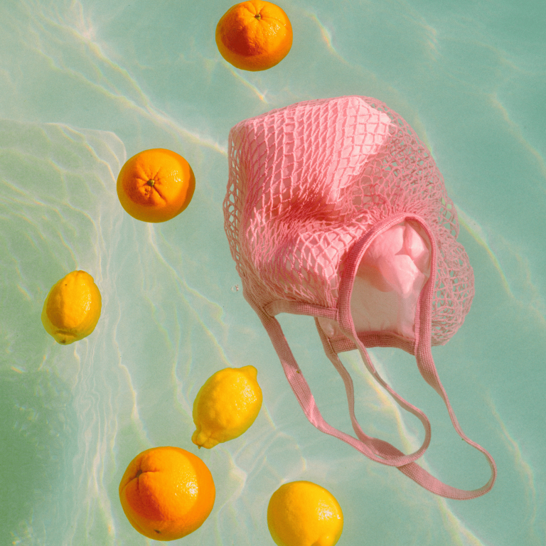 a pool with an empty pink string shopping bag with oranges and lemons floating beside it