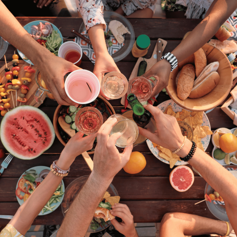 group of people at a laden picnic table clinking their drinks glasses together